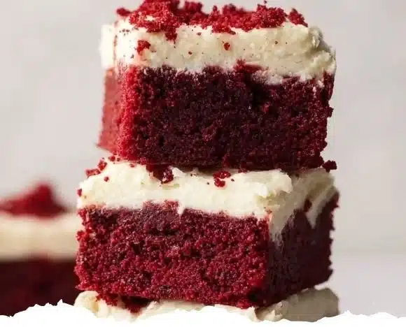 Red velvet brownies with cream cheese frosting on a white plate.