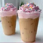 A beautifully crafted celebratory iced latte with whipped cream and a festive straw.