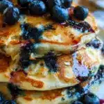 Stack of fluffy blueberry pancakes with fresh blueberries and syrup